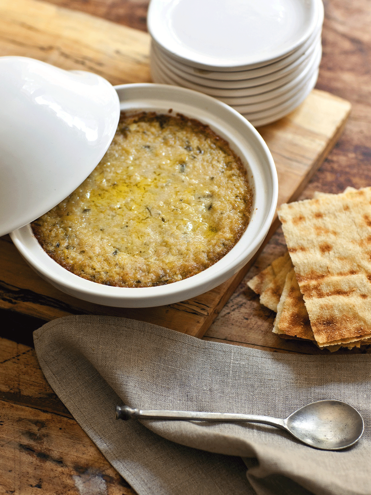 Baked artichoke lemon pesto dip served in a white ceramic dish with flatbread crackers – Bella Cucina