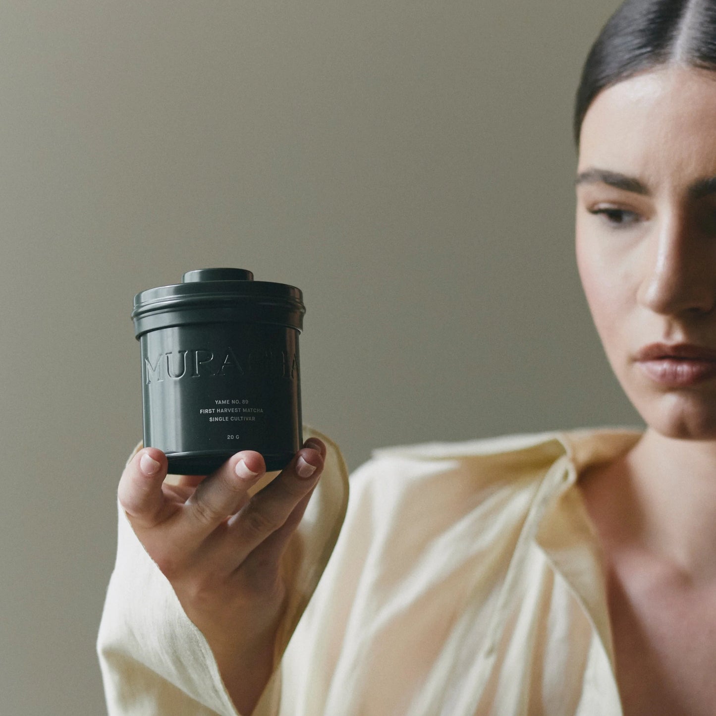 Woman holding a black container with 'MURACOL' branding against a neutral background