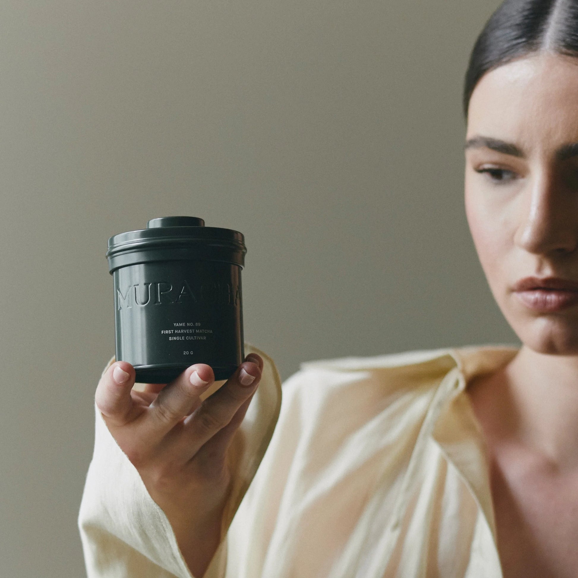 Woman holding a black container with 'MURACOL' branding against a neutral background