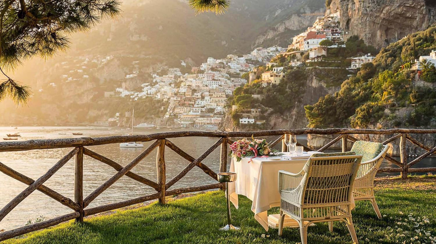 Dining table set for two with a scenic view of a coastal town and mountains.