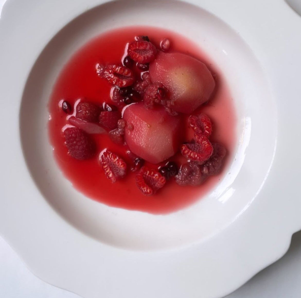 Roasted Seckel Pears with Raspberries on a white plate with a spoon beside it.