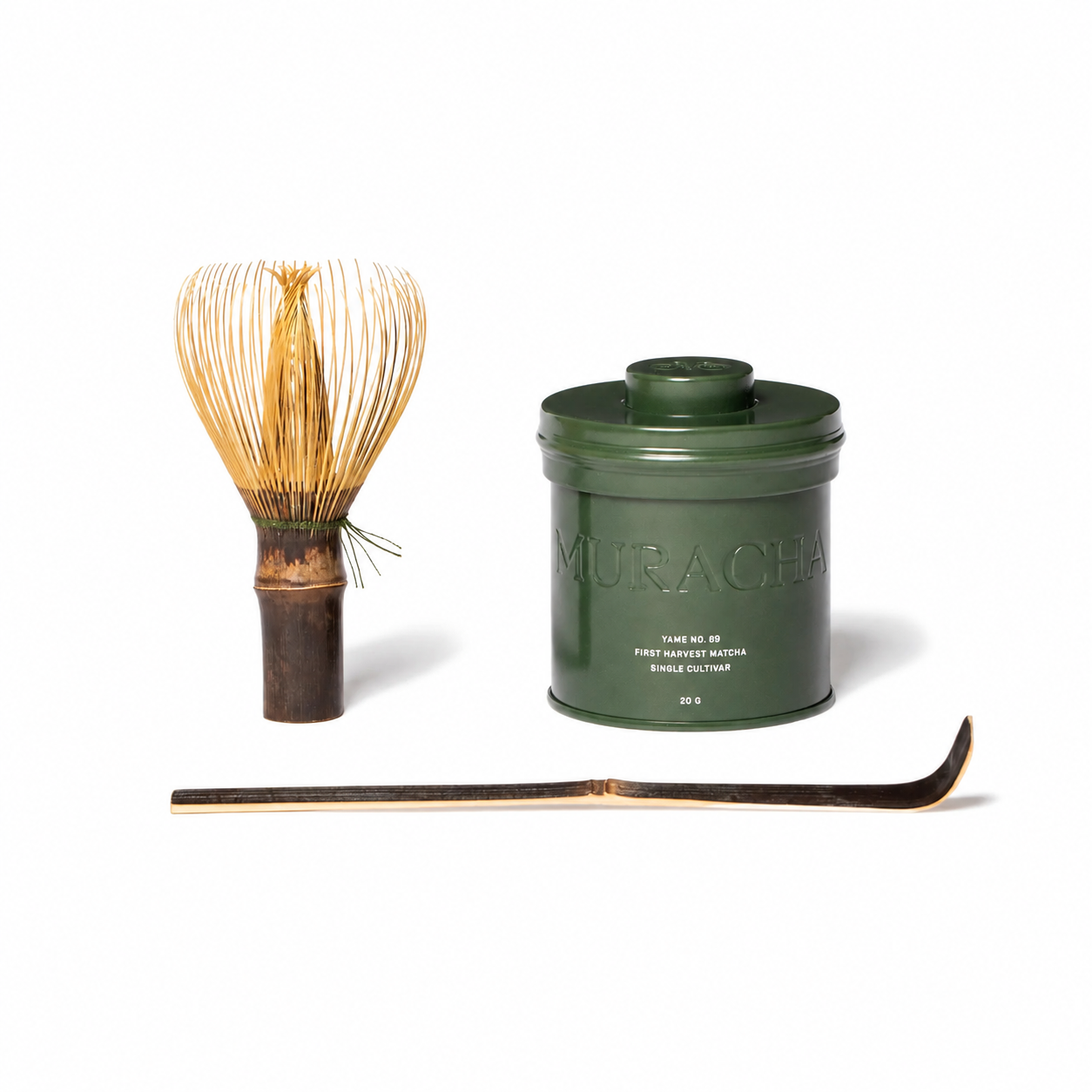 A traditional Japanese matcha tea set on a white background, featuring a dark green metal canister embossed with 'MURACHA', a bamboo whisk, and a bamboo scoop.