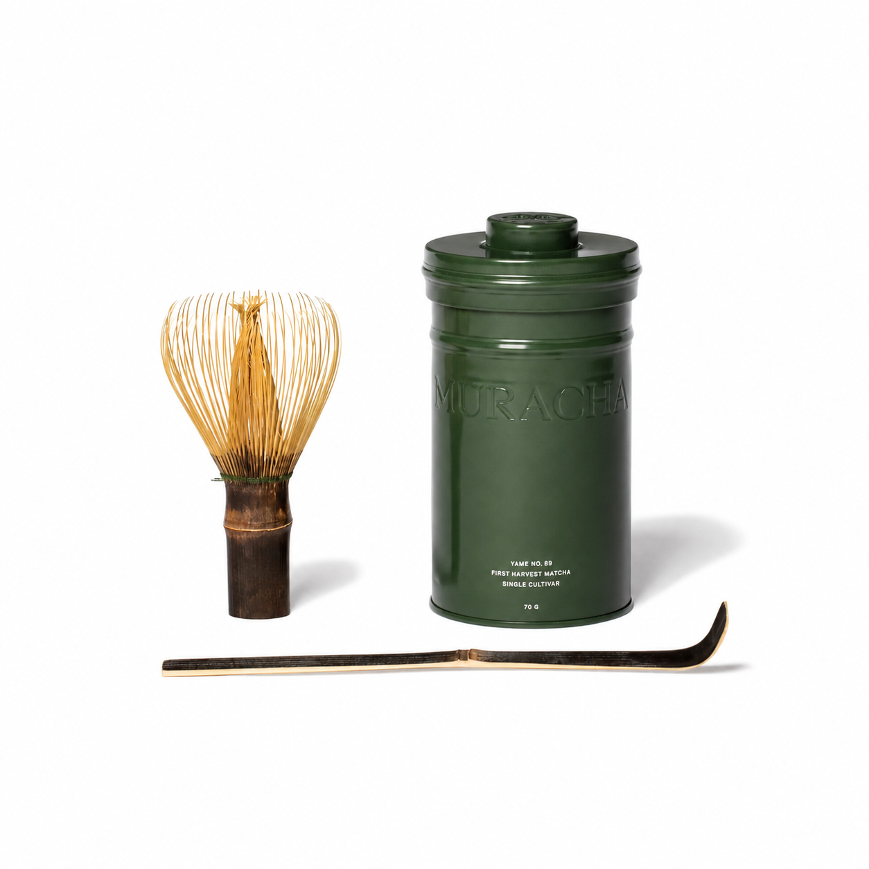 A green ceramic matcha tea canister with embossed lettering, a bamboo whisk, and a bamboo scoop arranged on a clean white background.