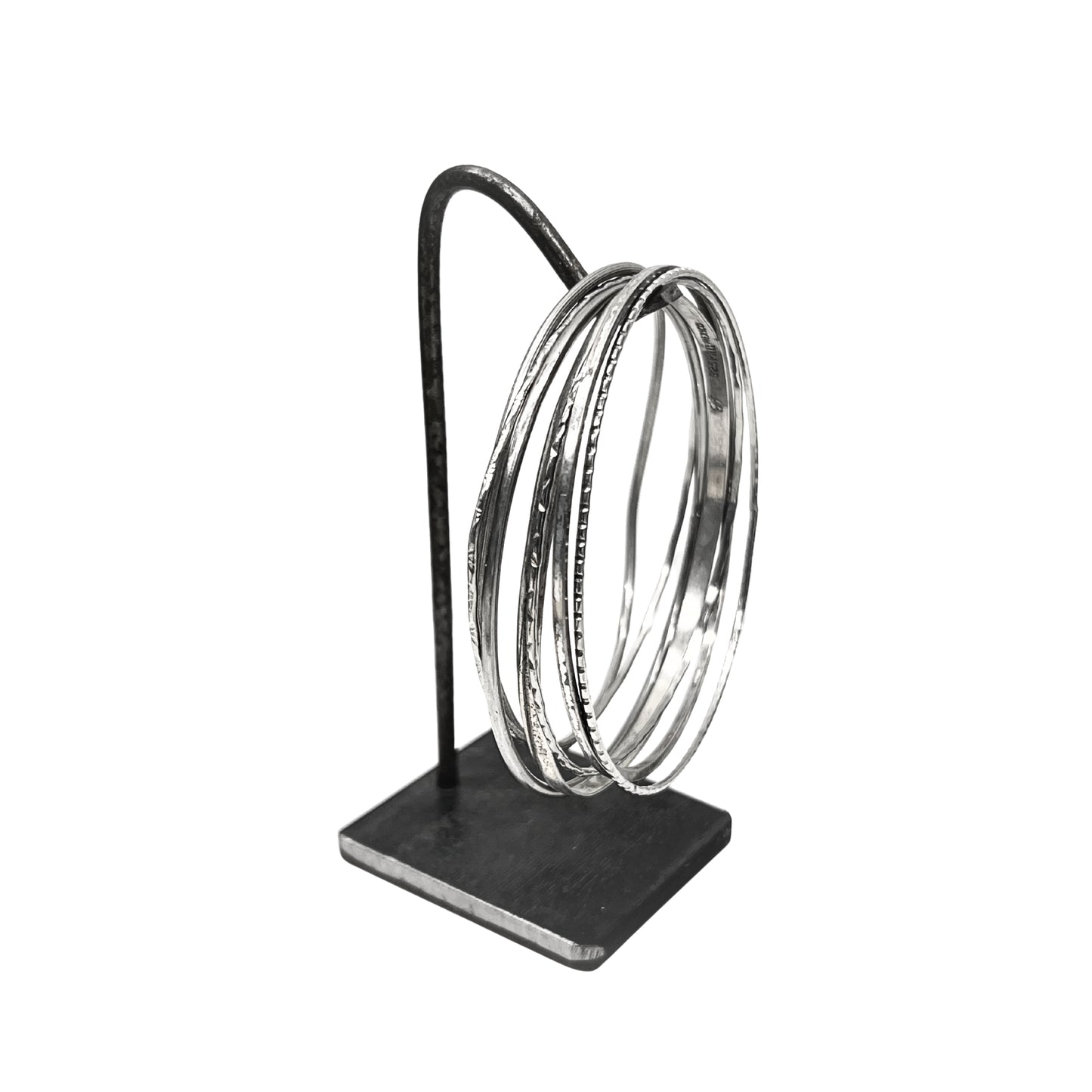 Set of silver bangles on a black stand against a white background