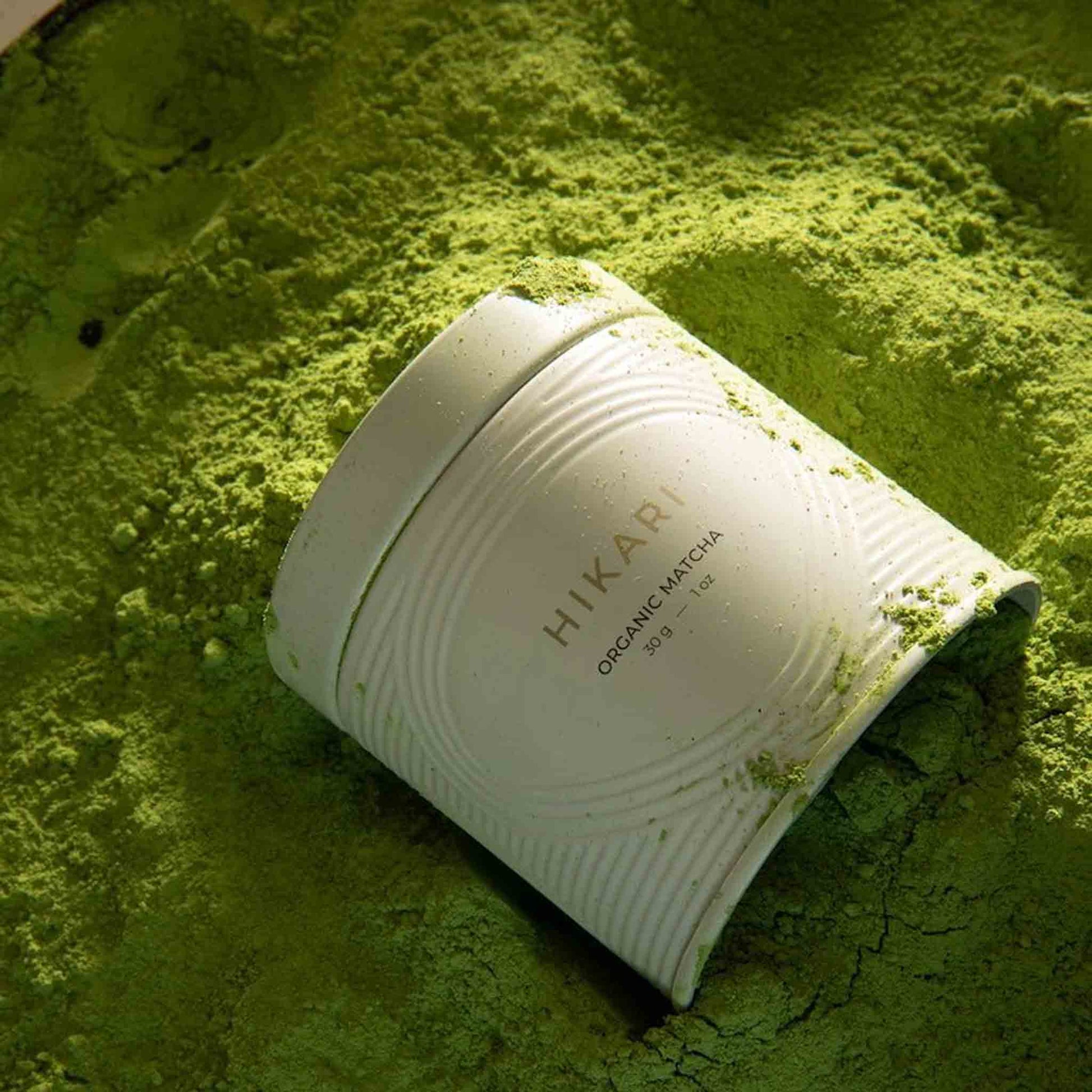 HIKARI Matcha Tea tin lying in vibrant green matcha powder, showcasing its fine ceremonial-grade quality and rich color.