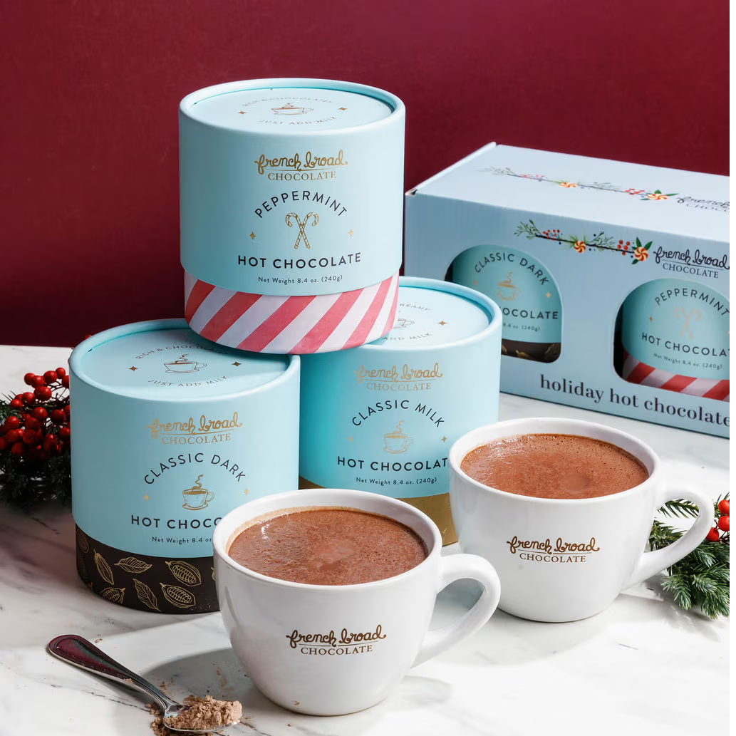 Hot chocolate products including tins and mugs on a table with a red background